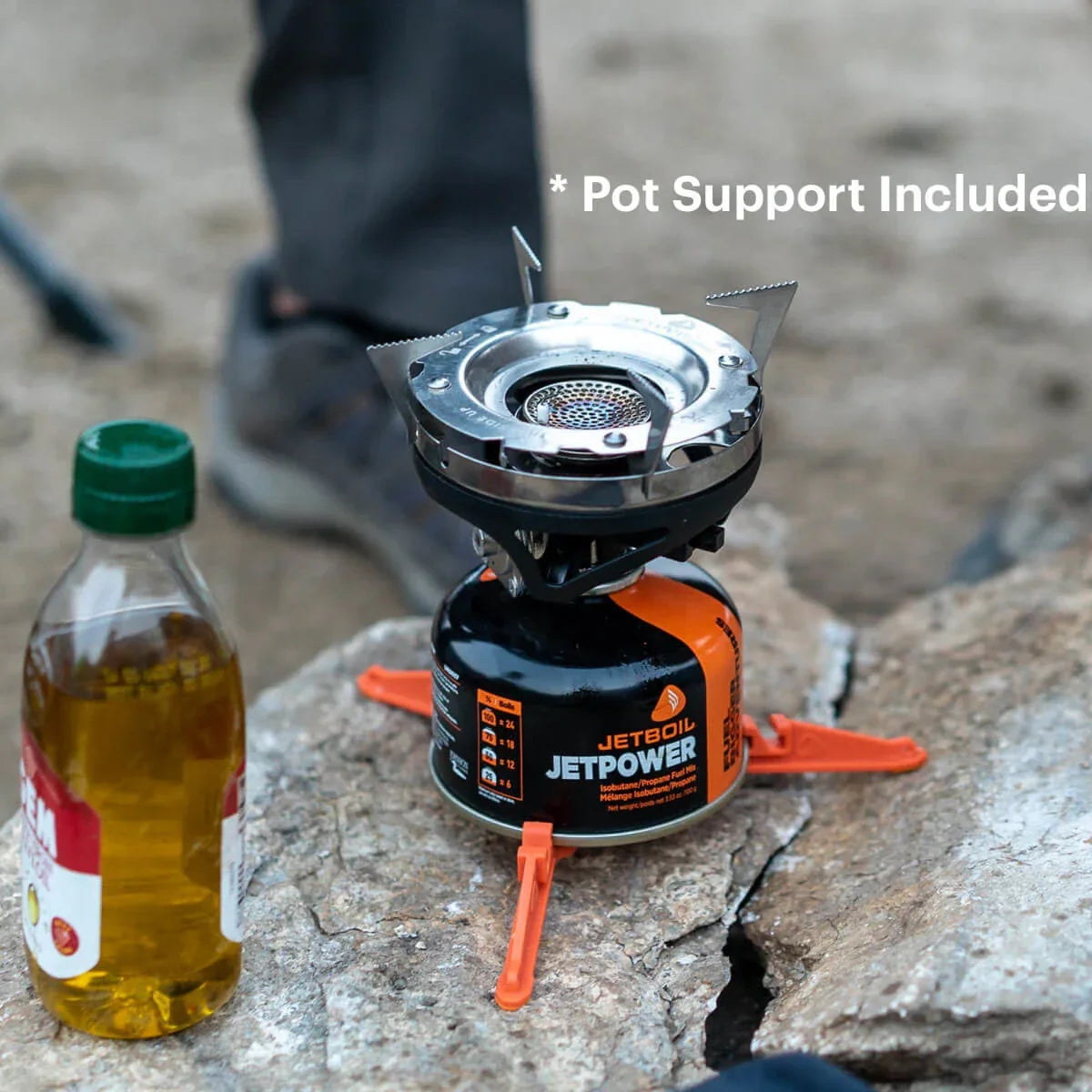 Portable stove with pot support on a rock, next to a bottle of oil, with 'Pot Support Included' text.