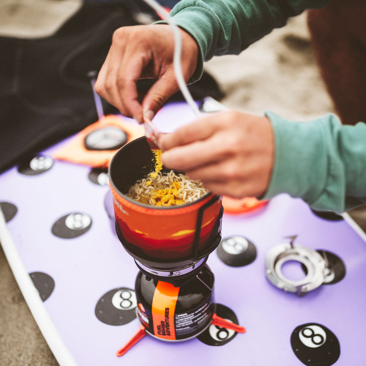Person preparing food over a camping stove on a purple mat with numbers.