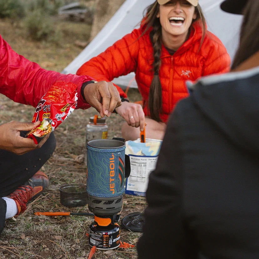 People camping outdoors, preparing food with a Jetboil stove.