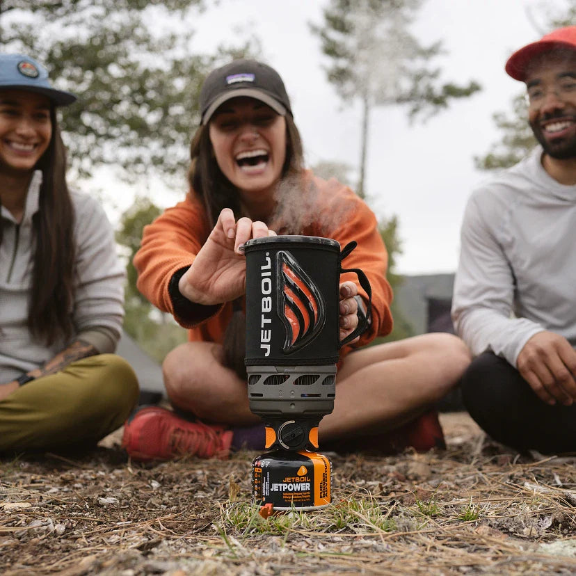 Person holding a Jetboil stove outdoors with two others in the background