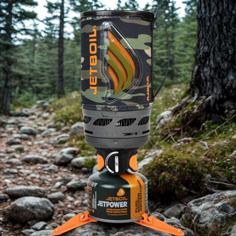 Camouflage Jetboil stove on a forest floor with trees and rocks in the background