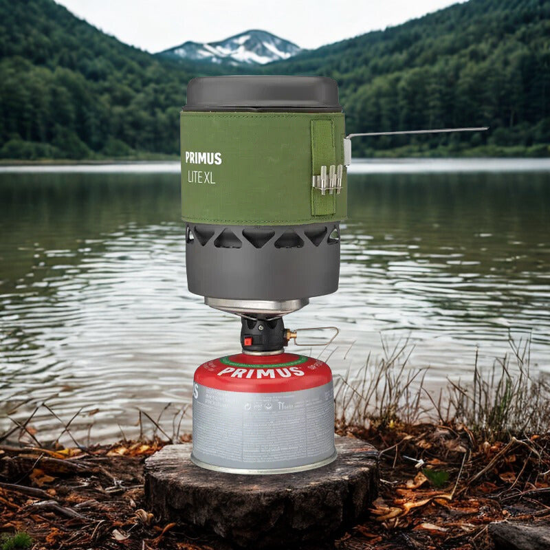 Primus Lite XL camping stove on a stump by a lake with mountains in the background