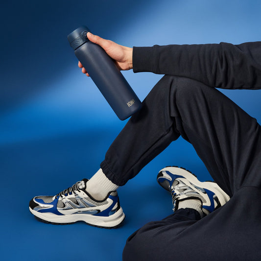 Person sitting on a blue background holding a blue water bottle.