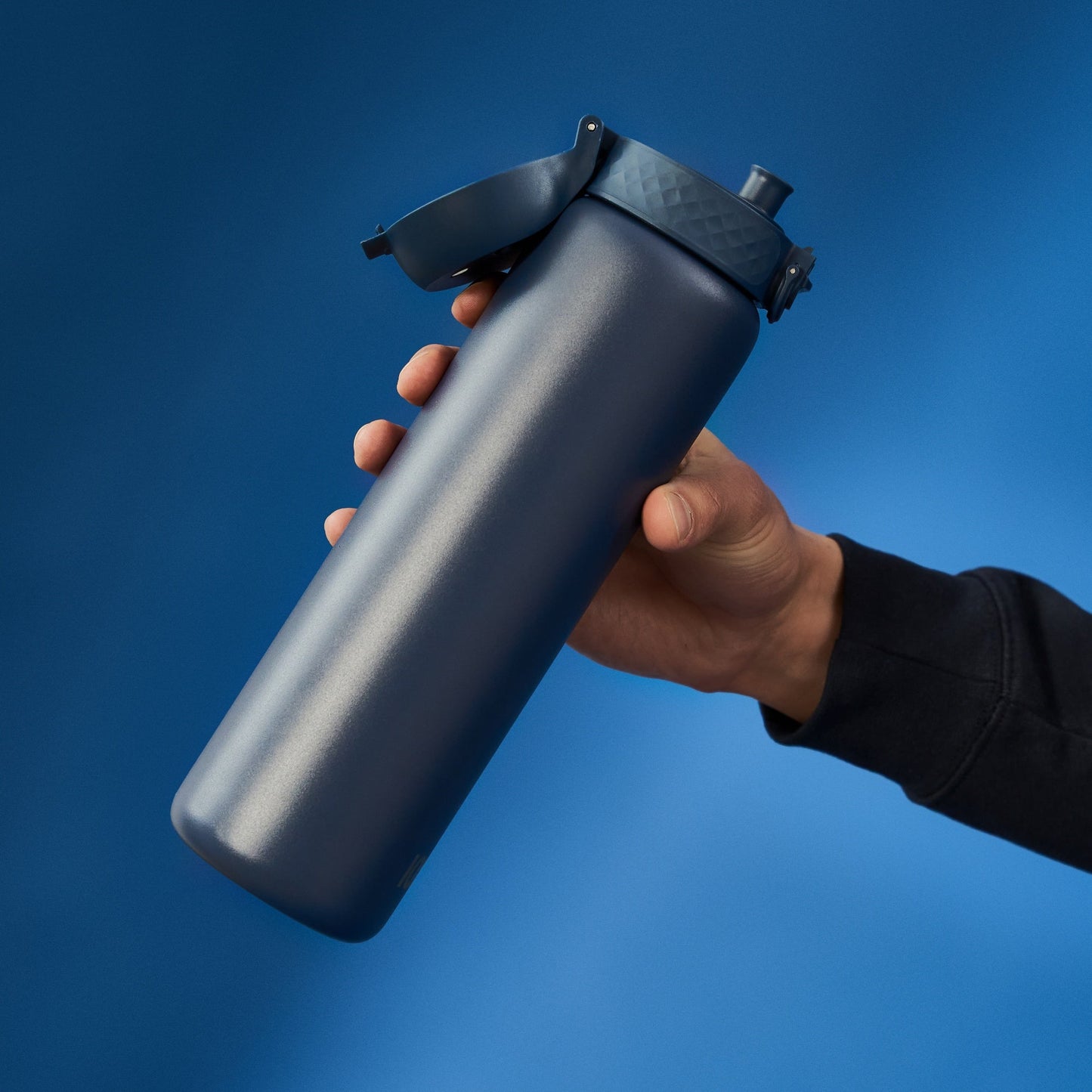 Hand holding a black water bottle against a blue background