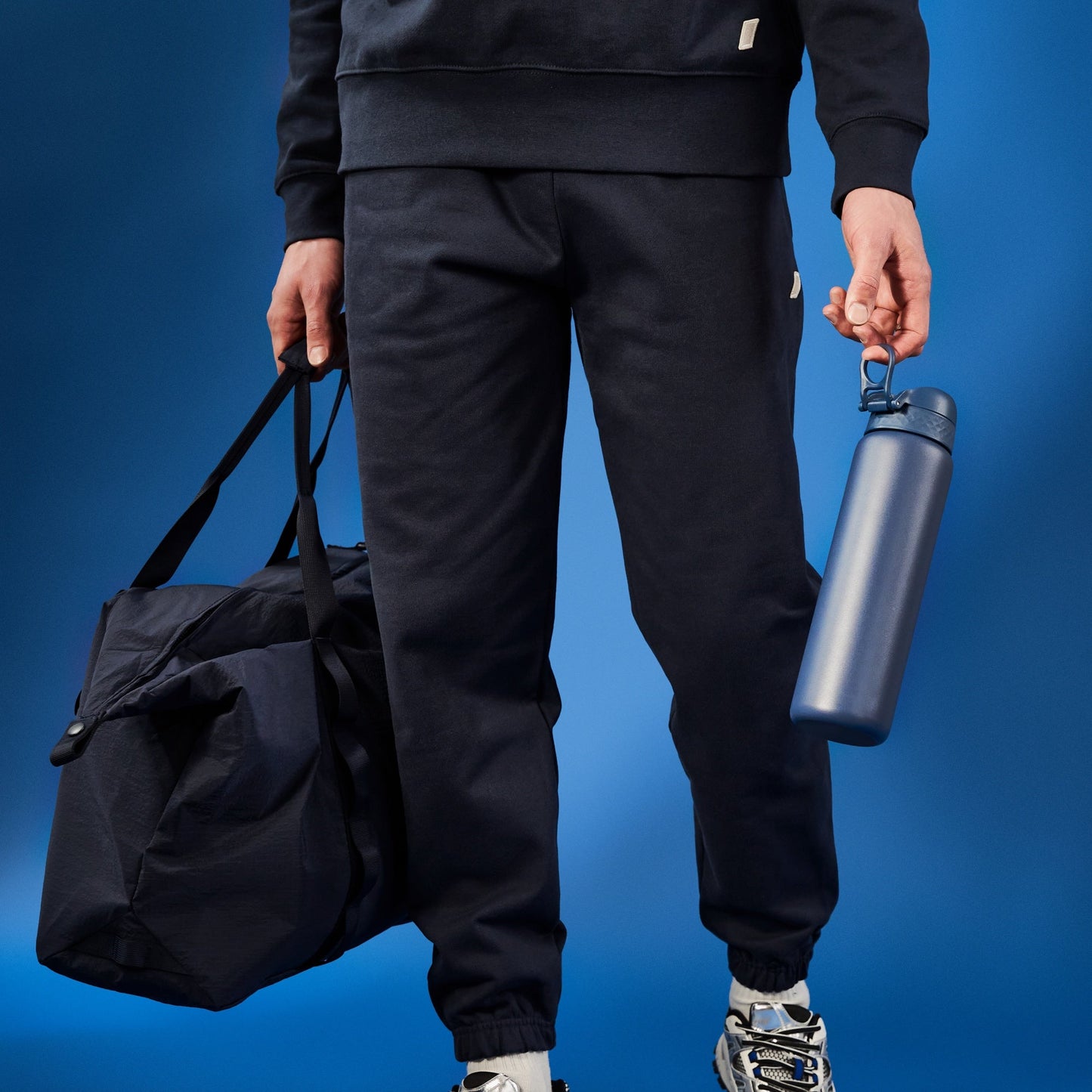 Person holding a black duffel bag and a blue water bottle against a blue background