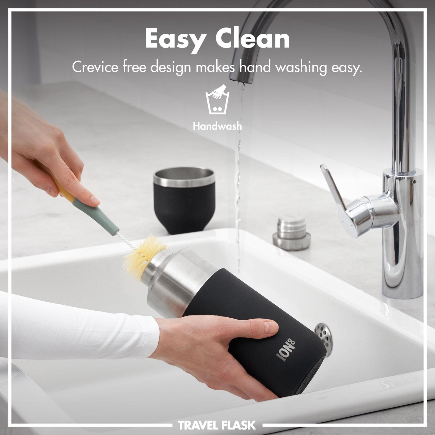 Person cleaning a travel flask with a brush under running water in a sink.