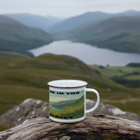 White enamel mug with Lake District landscape and black text on rustic wooden surface outdoors.