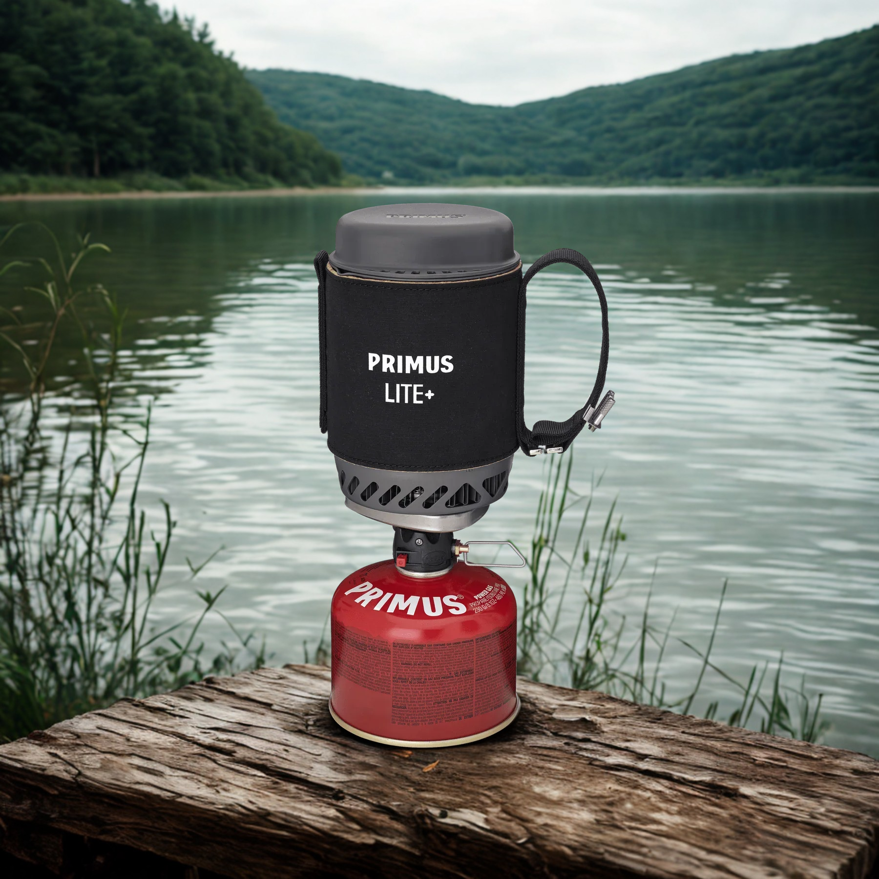 Primus Lite+ camping stove with red canister on a log by a lake