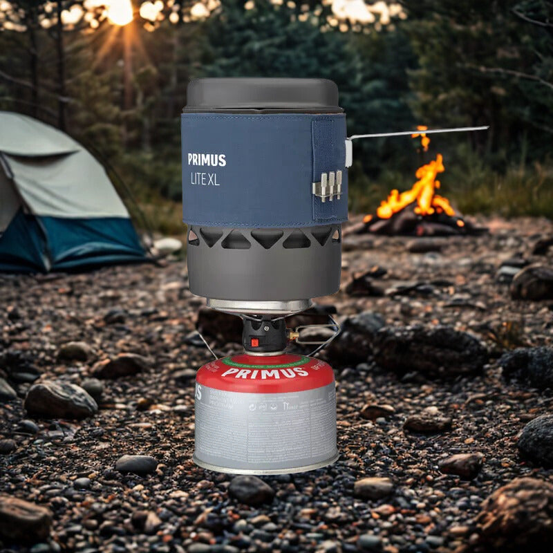 Primus Lite XL camping stove on a campsite with a fire and tent in the background