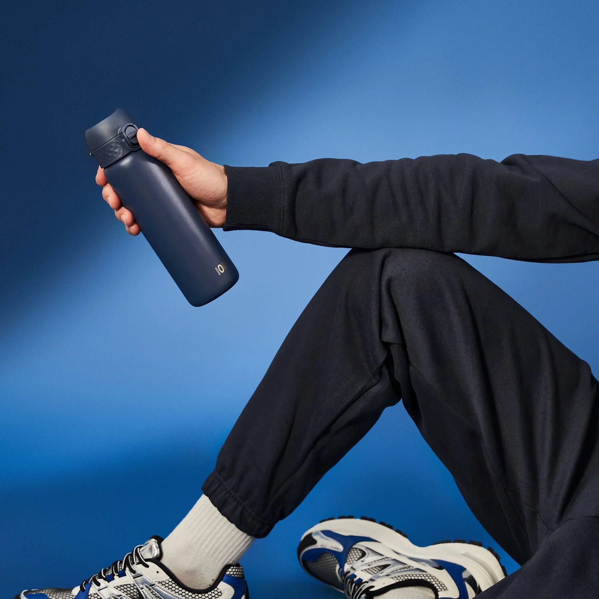 Person holding a black water bottle against a blue background