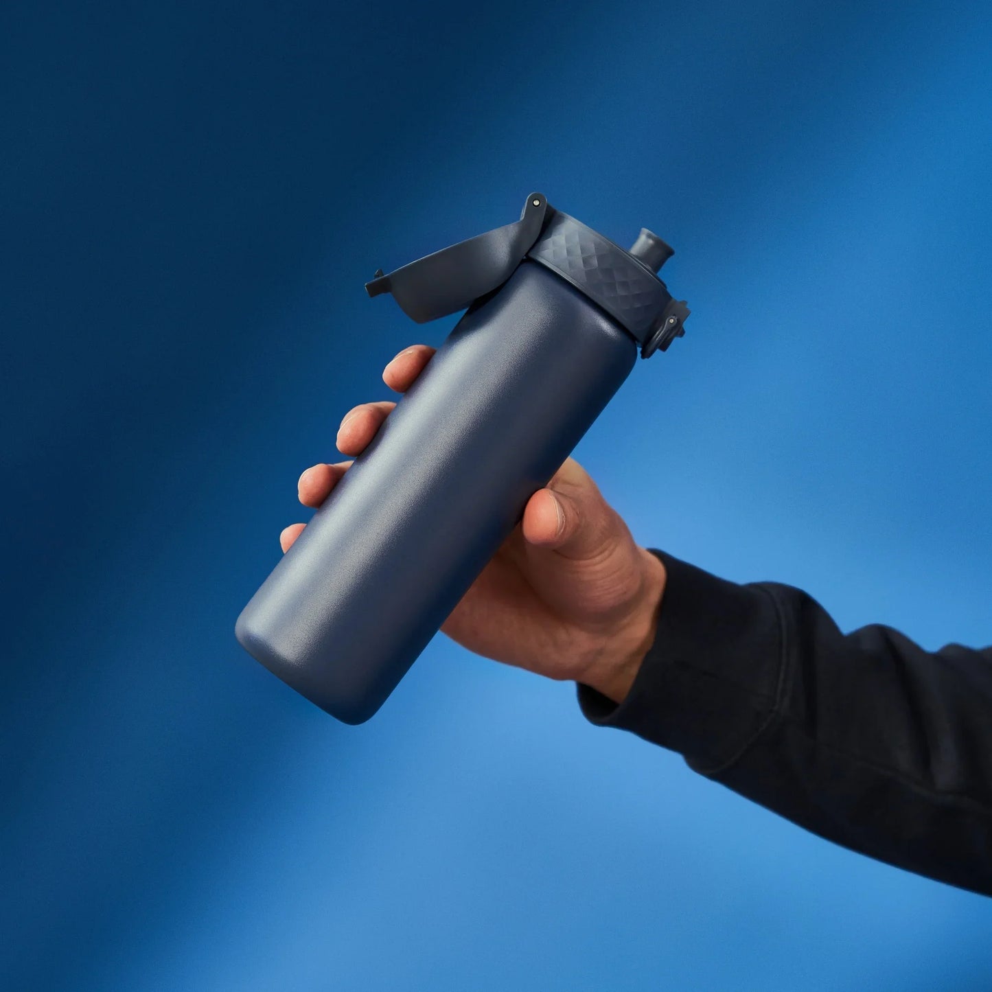 Hand holding a black spray bottle against a blue background