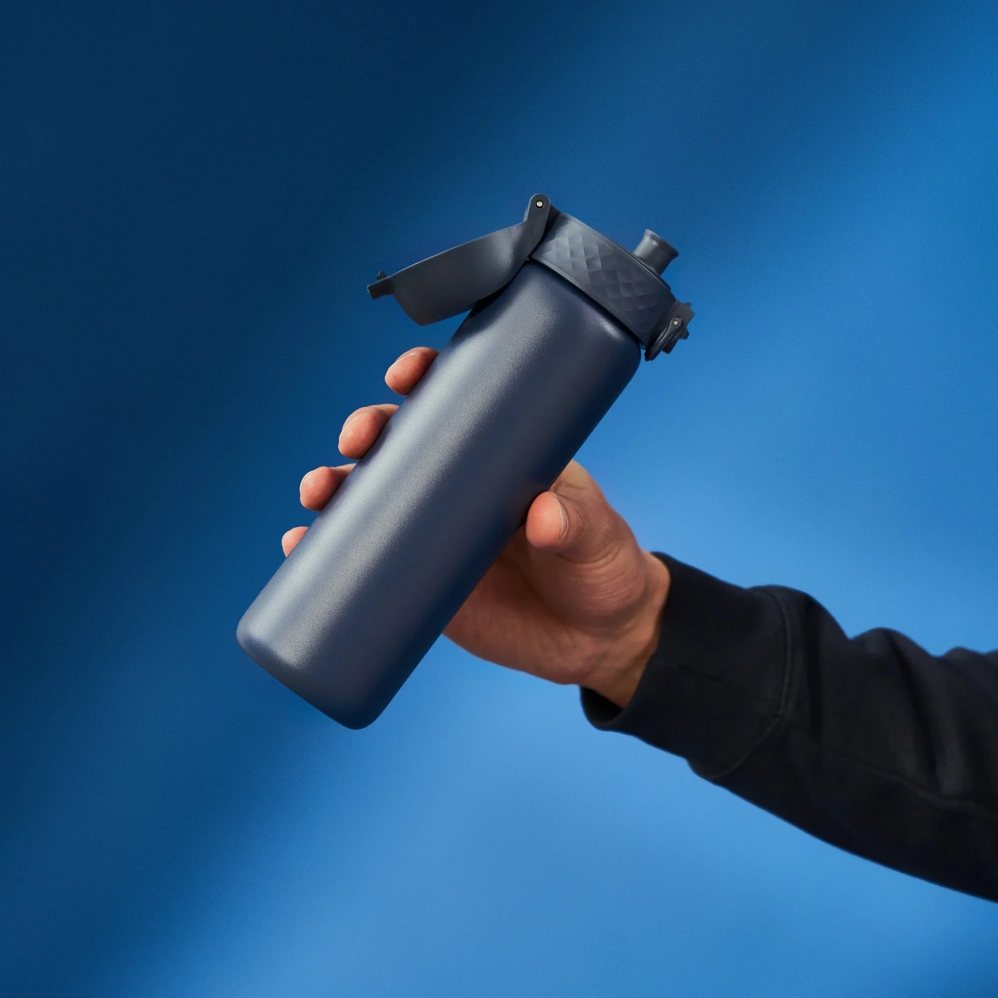 Hand holding a black spray bottle against a blue background