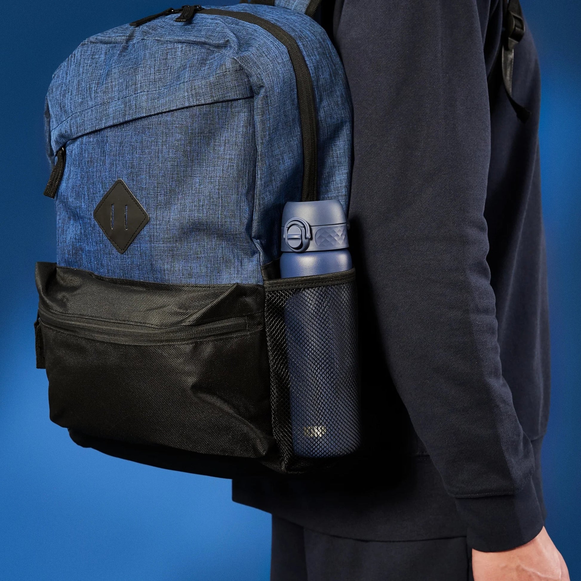 Person wearing a blue and black backpack with a water bottle in a pocket against a blue background