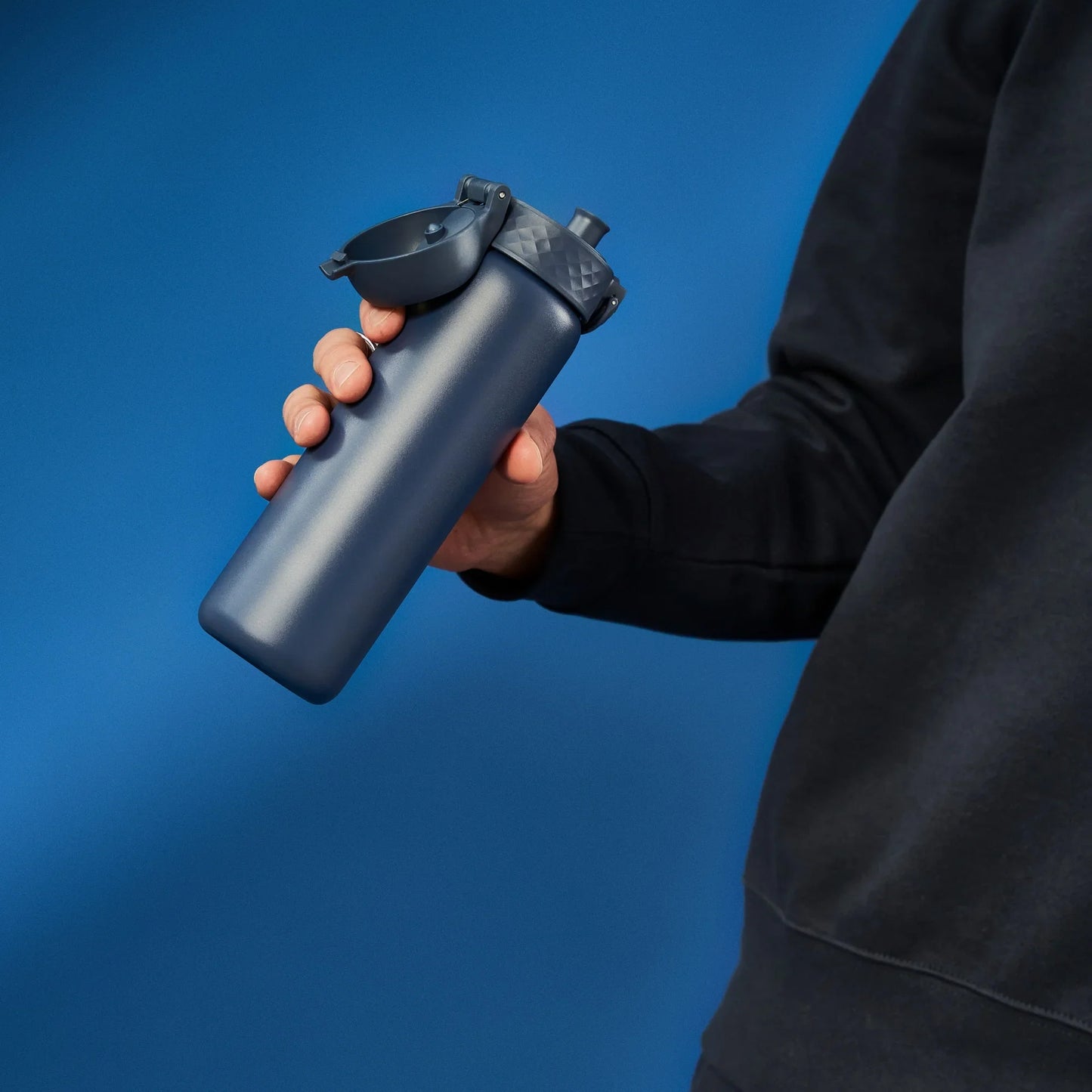 Person holding a black water bottle against a blue background