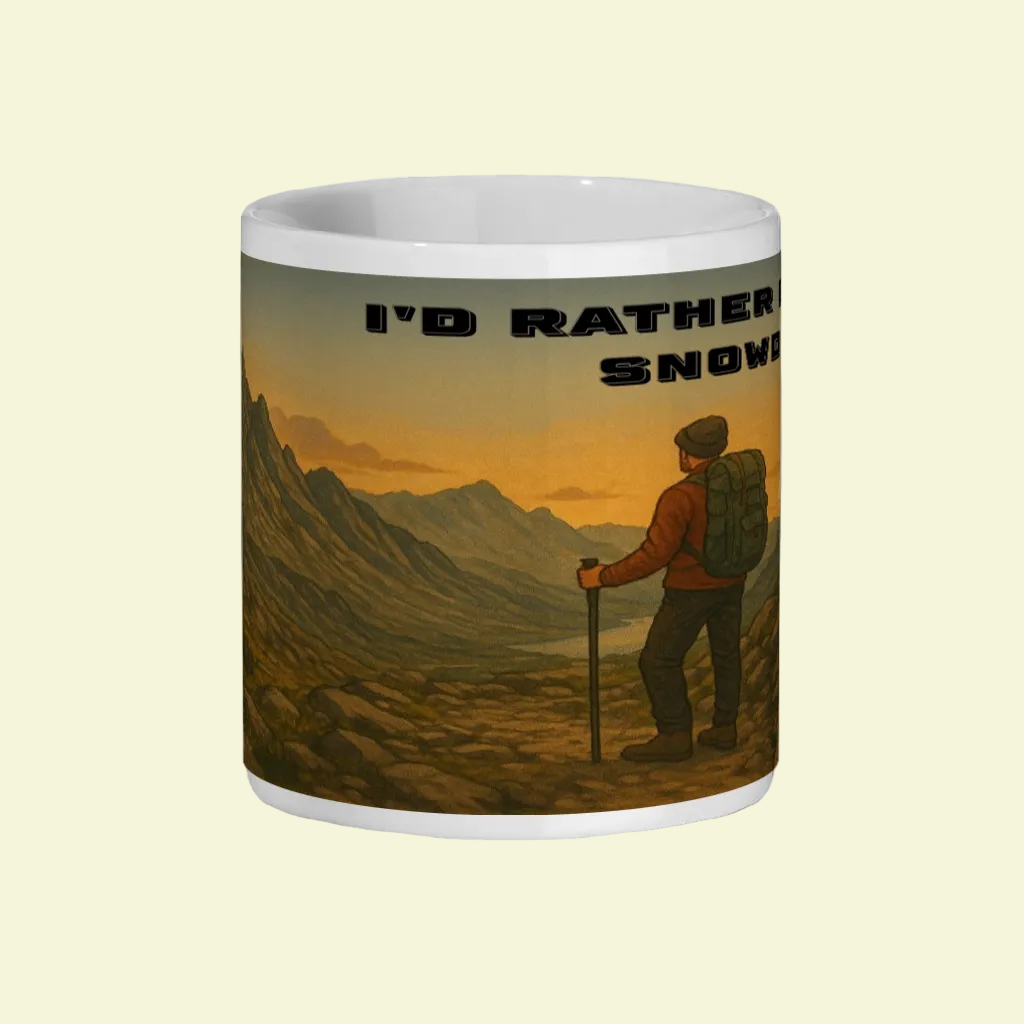 White ceramic mug with illustration of hiker overlooking mountain valley at sunset and text "I'd Rather Be in Snowdonia".