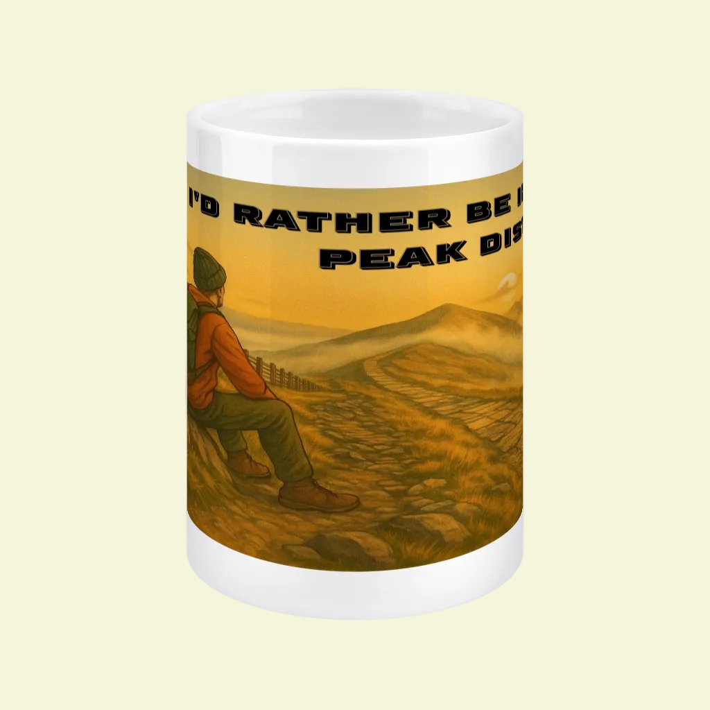 White ceramic 15oz mug with illustration of hiker sitting on grassy hill and text "I'd Rather Be in the Peak District".