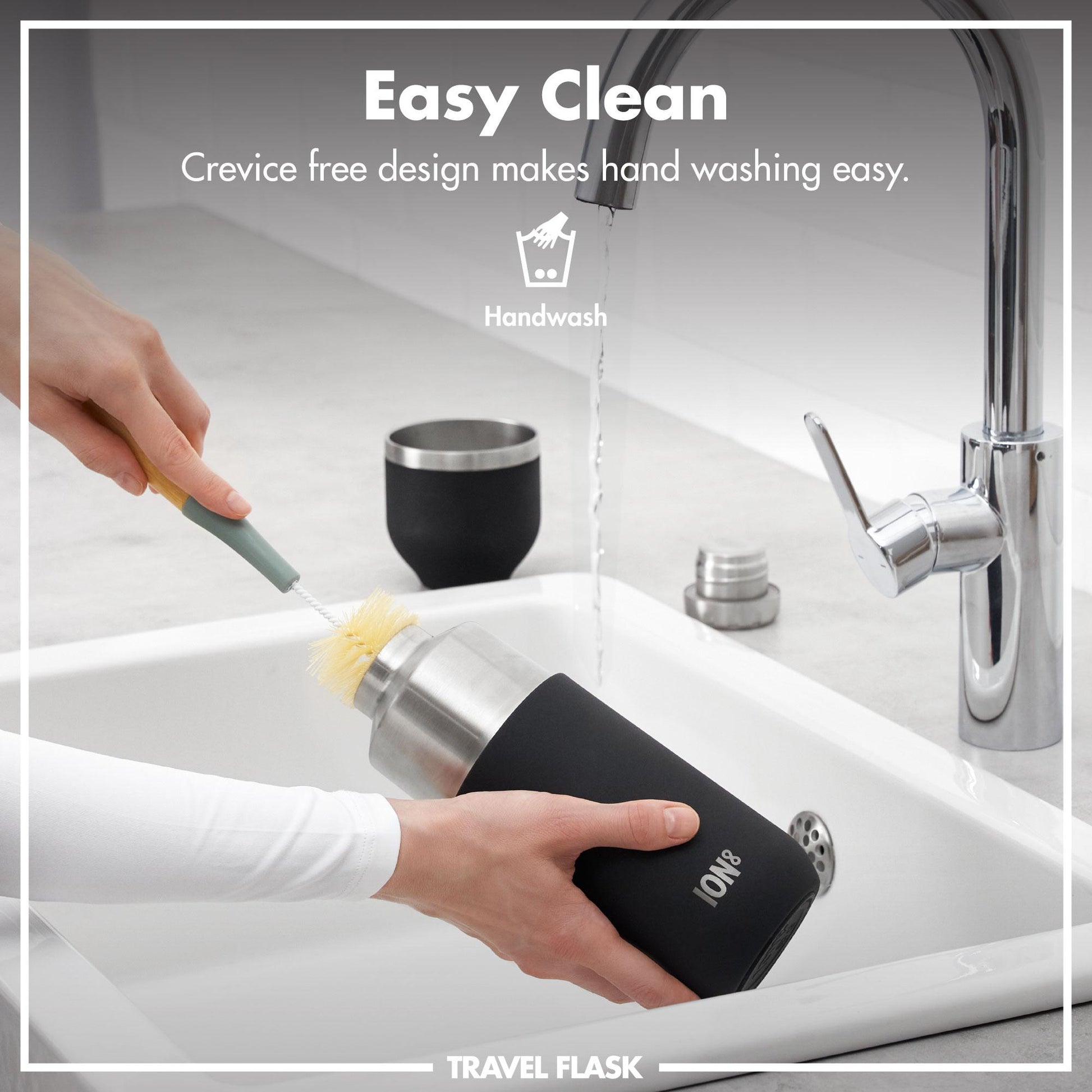 Person cleaning a travel flask with a brush under running water in a sink.
