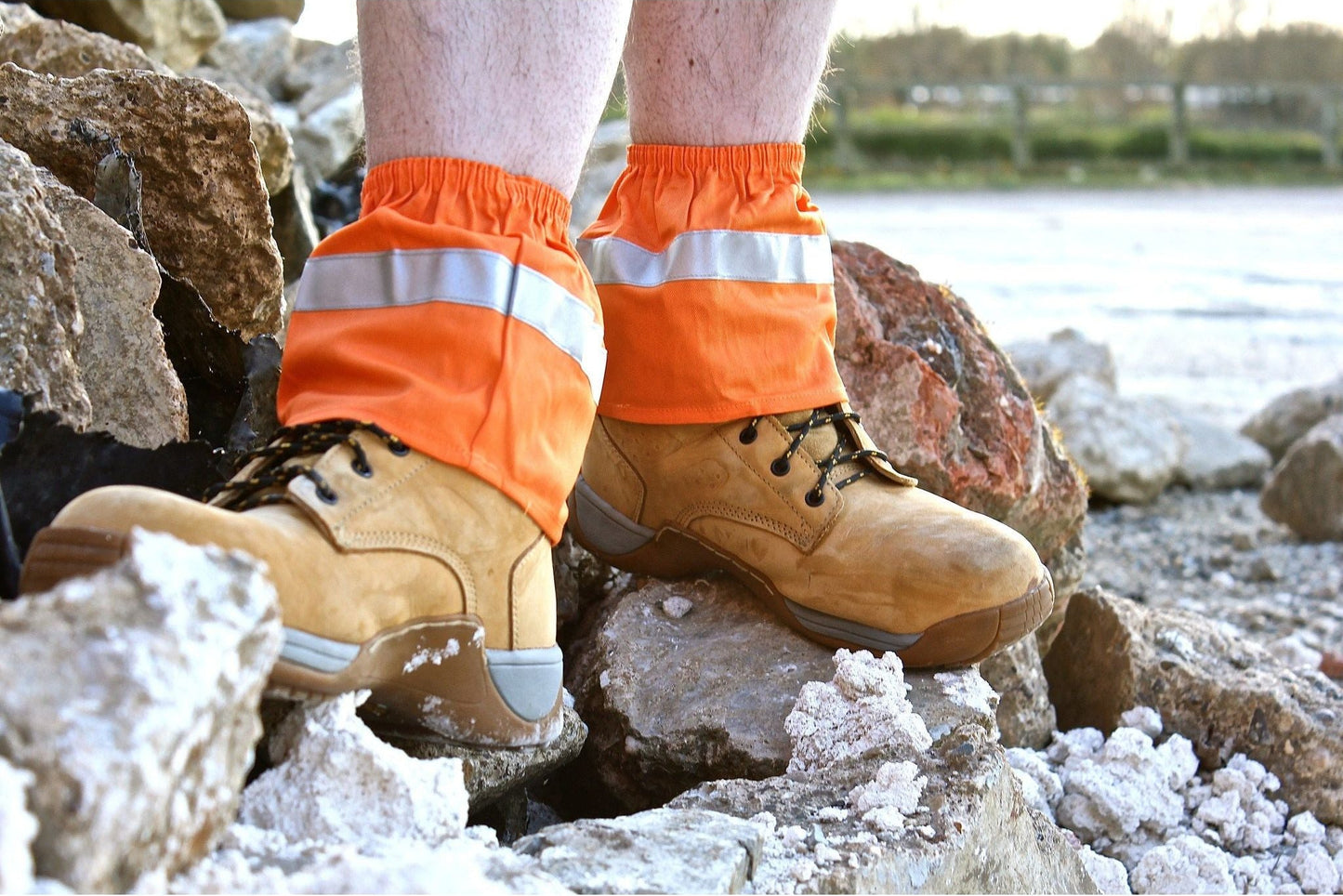 Person wearing orange reflective gaiters and brown work boots on a rocky surface.