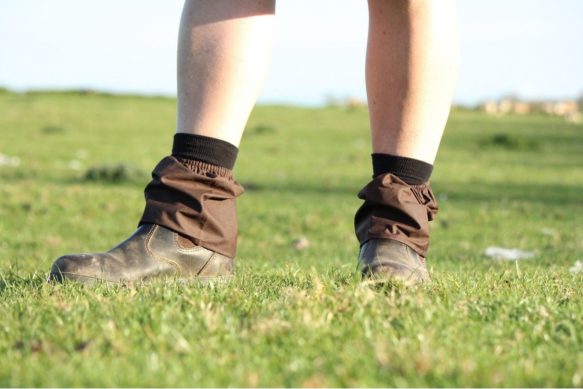 Person wearing brown boots and gaiters on a grassy field