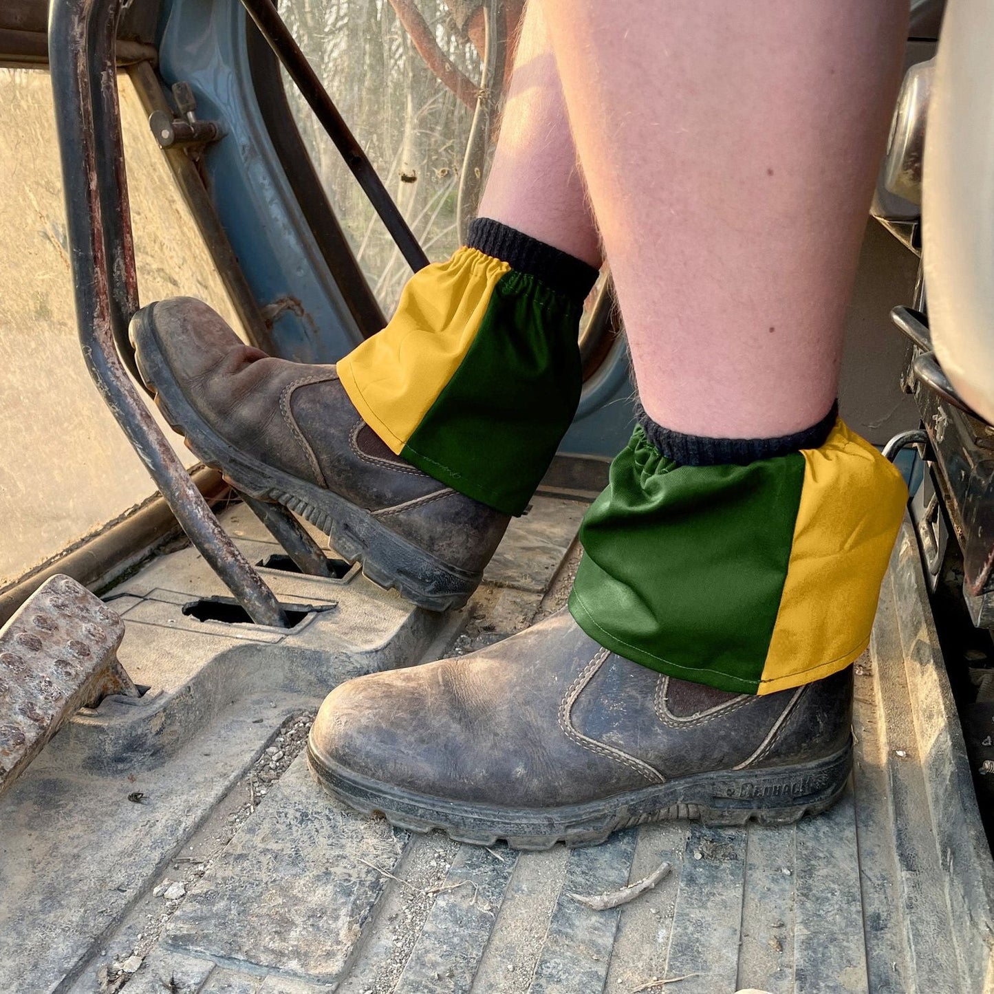 Person wearing green and yellow leg gaiters on a construction site.