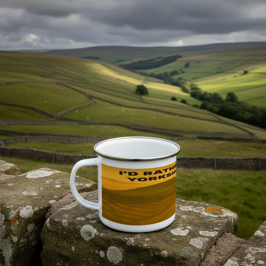 White enamel mug with yellow band and black text "I'd Rather Be in the Yorkshire Dales" on stone wall outdoors.