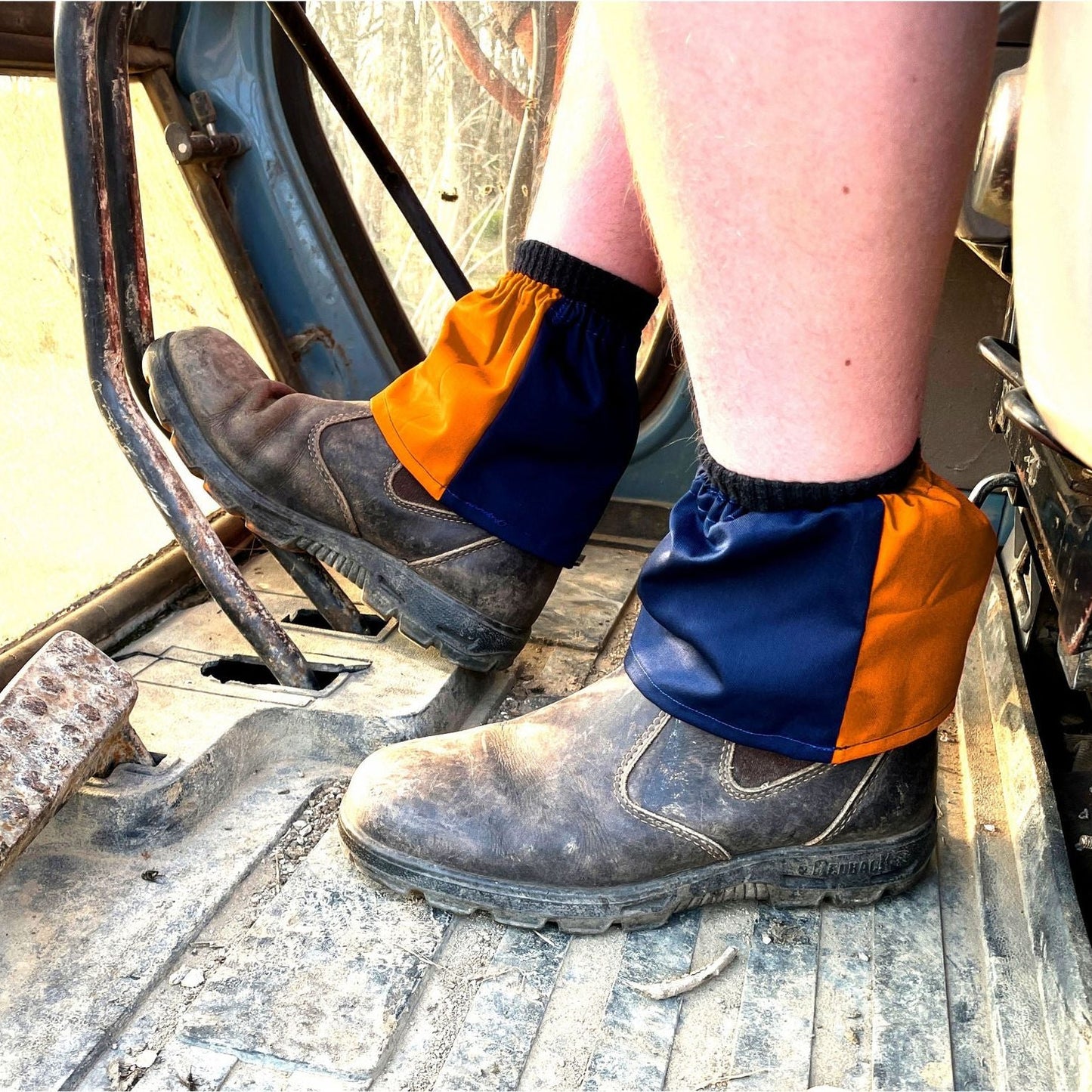 Person wearing work boots with orange and blue gaiters on a construction site.