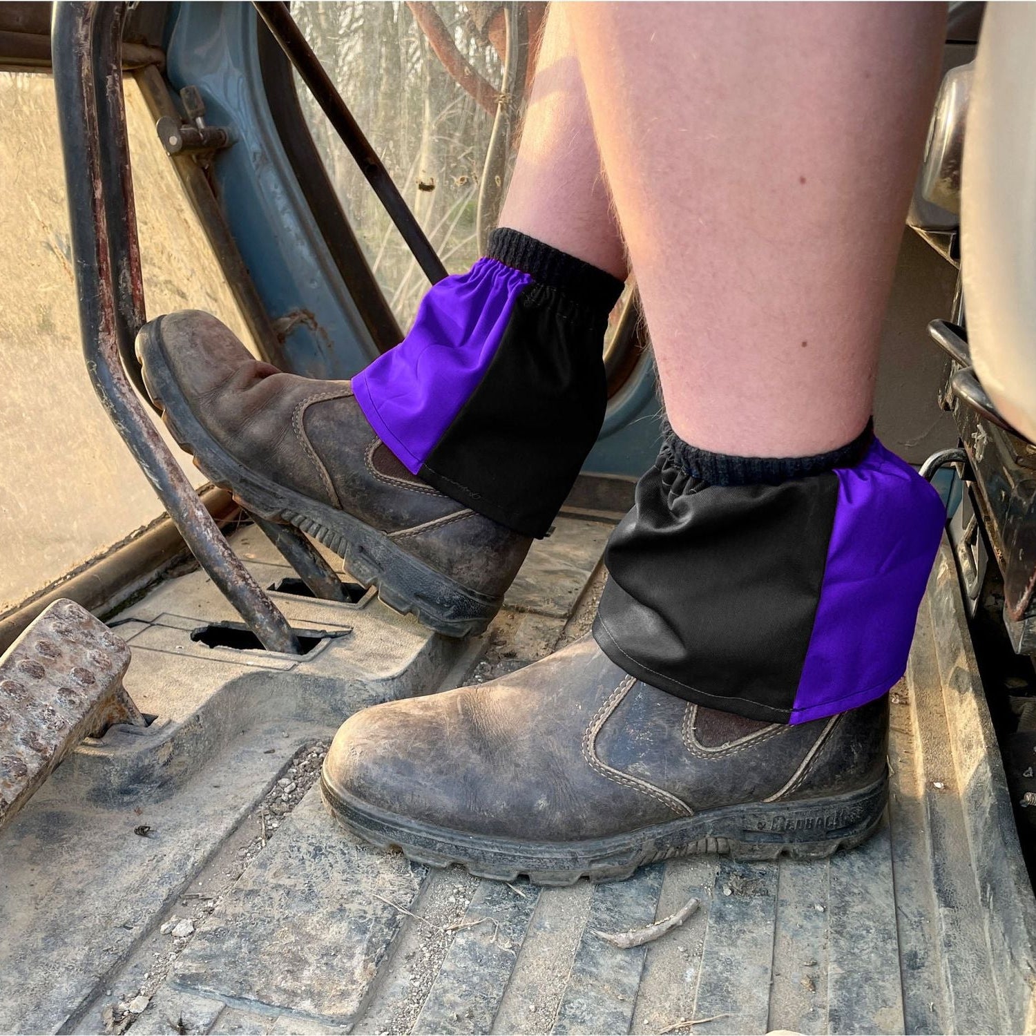 Person wearing black work boots with purple gaiters on a construction site.