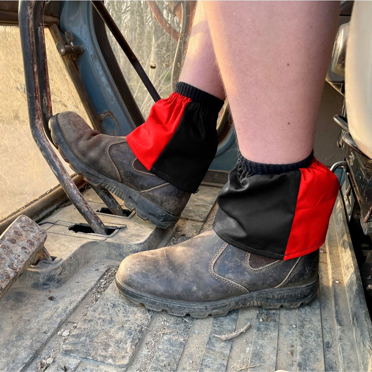 Person wearing black work boots with red gaiters on a construction site.