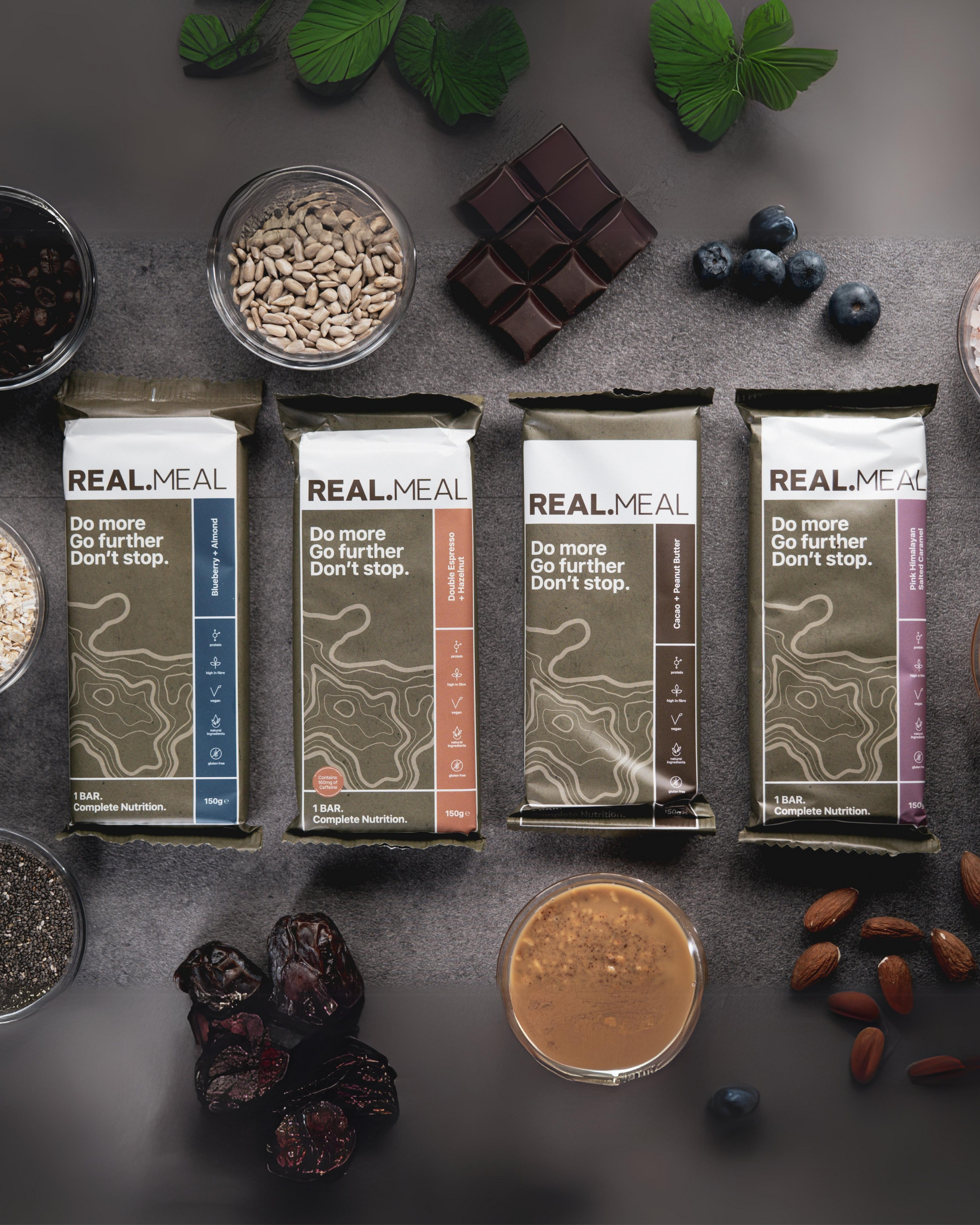 Real Meal meal replacement bars on a dark surface with various ingredients.