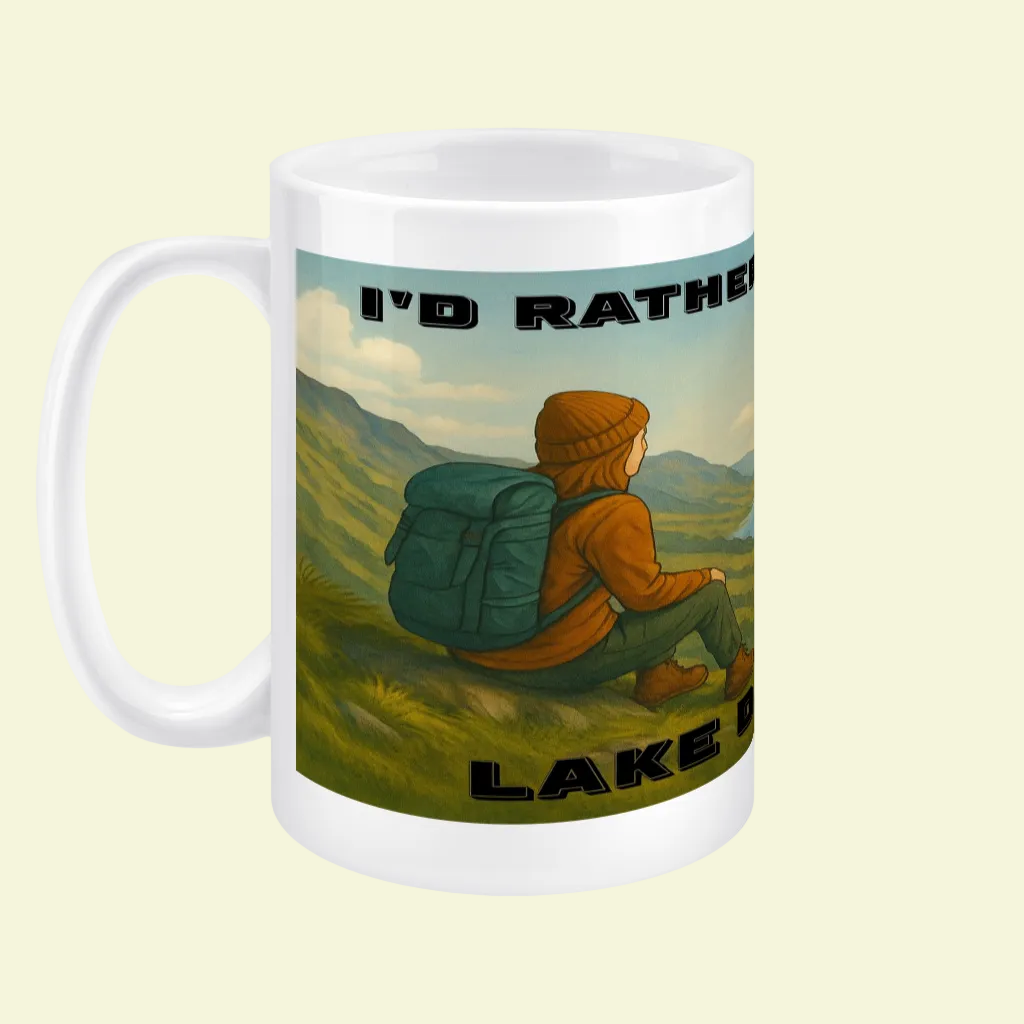 White ceramic mug with illustration of a hiker in an orange jacket overlooking Lake District hills.
