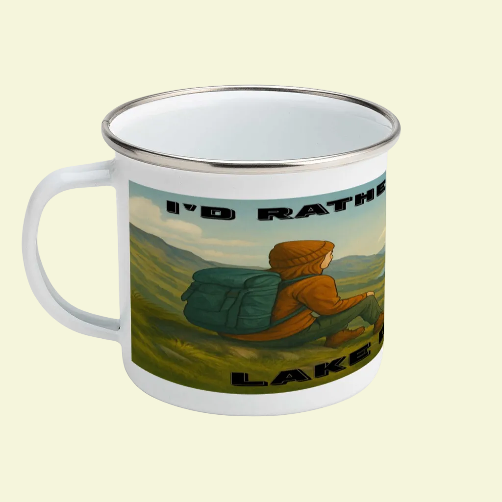White enamel mug with silver rim, featuring illustration of a hiker in orange jacket and backpack against green hills, and.