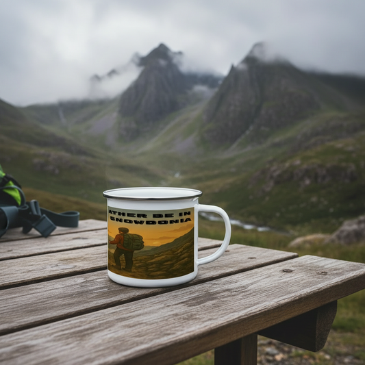 White enamel camping mug with "I'd Rather Be in Snowdonia" text and mountain hiker graphic on wooden table.